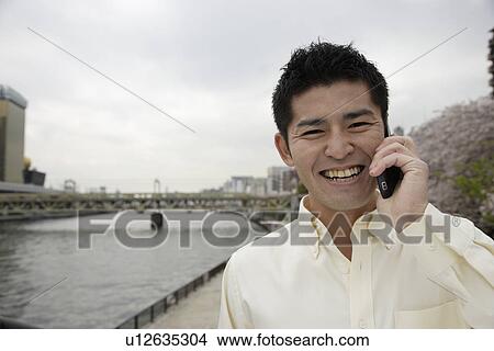 Picture - A smiling young man using cellphone. Fotosearch