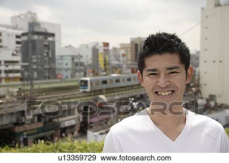 Stock Photo - A young man smiling with buildings and train in background. Fotosearch