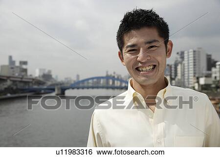 Stock Photograph - A young man standing with river in background. Fotosearch