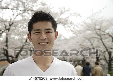 Stock Image - A young man standing with trees in background. Fotosearch