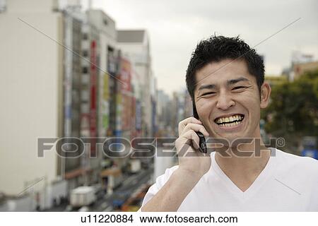 Picture - A young man using cellphone with buildings in background. Fotosearch