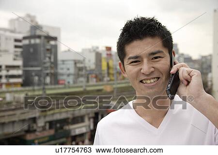 Stock Image - A young man using cellphone with buildings in background. Fotosearch