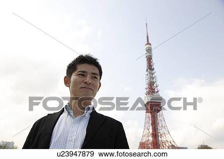 Stock Photo - Low angle view of a young man with tower in background. Fotosearch