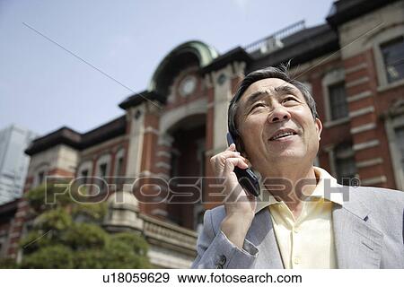 Stock Photo - Low angle view of a senior man using mobile phone. Fotosearch