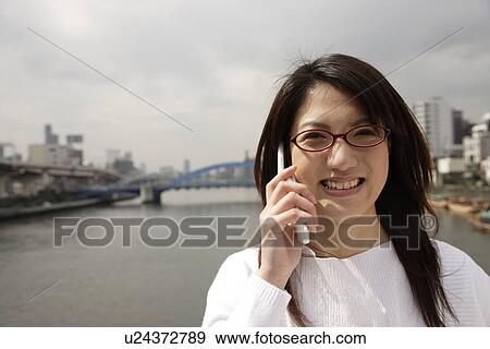 Stock Photo - Close-up of a young woman using mobile phone with river in background. Fotosearch