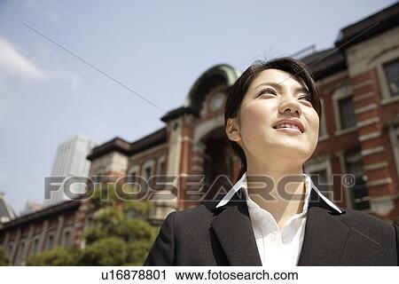 Stock Image - Low angle view of a smiling young woman standing outside the building. Fotosearch