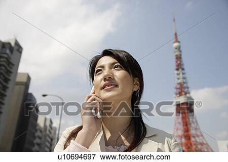 Stock Photo - Low angle view of a young woman using mobile phone. Fotosearch