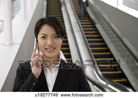 Stock Photo - Portrait of a smiling young woman using mobile phone on the moving stairway. Fotosearch