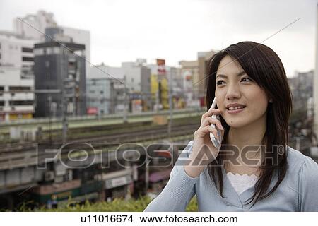 Picture - View of a smiling young woman using mobile phone. Fotosearch