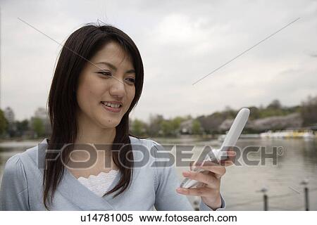 Stock Photography - View of a smiling young woman using mobile phone. Fotosearch