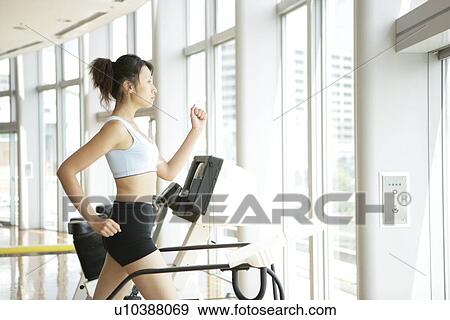 Stock Photo - A young woman jogs on a walker as she exercises in a well equipped gym. Fotosearch