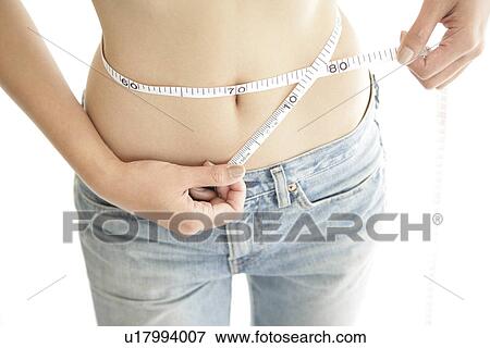 Stock Photo - A young woman measuring her waist with the help of a measure tape. Fotosearch