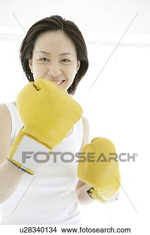A young woman smiles with the gloves on as she poses against the camera View Large Photo Image Picture - A young woman smiles with the gloves on as she poses against the camera. Fotosearch