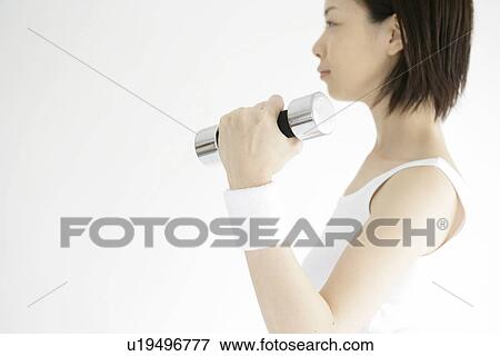 Side view of a young woman lifting the dumbbell View Large Photo Image Stock Photo - Side view of a young woman lifting the dumbbell. Fotosearch