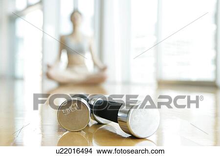 Picture - Two dumbbells placed closed to each other with a woman performing yoga is seen at the background. Fotosearch