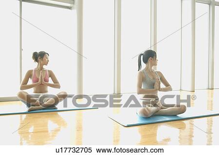 Stock Photography - Two young women cross their legs and sit while they perform yoga in the gym. Fotosearch