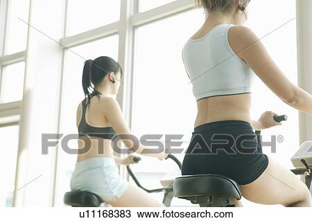 Stock Image - Two young women perform exercise in a well equipped gym. Fotosearch