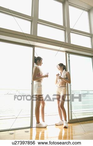 Two young women take a break from exercise as they stand near the sliding door View Large Photo Image Stock Photograph - Two young women take a break from exercise as they stand near the sliding door. Fotosearch