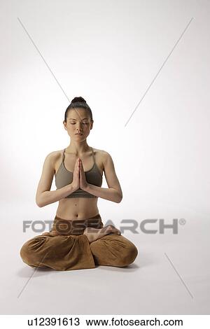 Stock Image - Front view of a young woman meditating in lotus position. Fotosearch