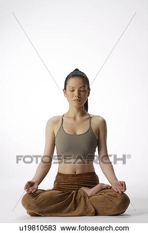 Stock Image - Front view of a young woman meditating in lotus position. Fotosearch