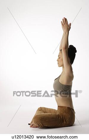 Stock Image - Side view of a young woman meditating in lotus position. Fotosearch
