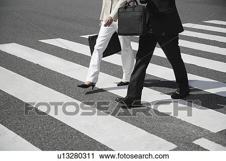 Stock Image - Cropped view of two people walking on crosswalk. Fotosearch