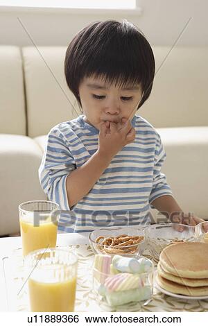 Stock Photograph - A boy at the table with some pancakes and snacks. Fotosearch