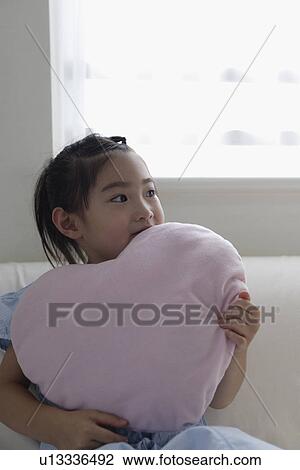 Stock Image - A girl holding a cushion on sofa. Fotosearch