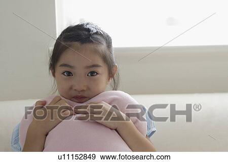 Stock Photo - A girl holding a cushion on sofa. Fotosearch