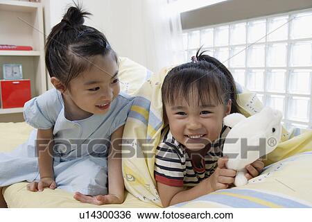 Stock Photograph - Sisters in bed with a soft doll. Fotosearch