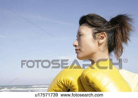 Stock Photo - A side view of a woman wearing boxing gloves seen near the sea . Fotosearch
