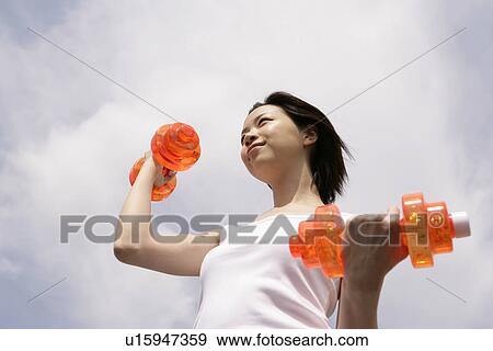 Stock Photo - A woman exercising as she lifts up the dumbbells. Fotosearch
