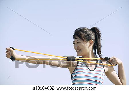 Stock Image - A woman working out as she stretches a rope tightly with her hands. Fotosearch