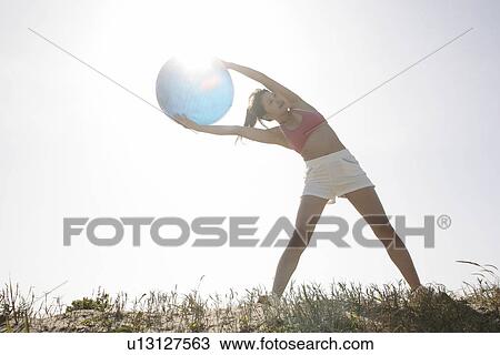 A young woman holds a huge ball as she bends from her abs while exercising under the sunlight View Large Photo Image Stock Image - A young woman holds a huge ball as she bends from her abs while exercising under the sunlight. Fotosearch