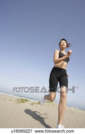 A young woman jogs along the beach on a bright sunny day View Large Photo Image Stock Photo - A young woman jogs along the beach on a bright sunny day. Fotosearch