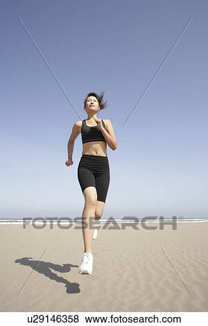 A young woman jogs along the beach on a bright sunny day View Large Photo Image Stock Photo - A young woman jogs along the beach on a bright sunny day. Fotosearch