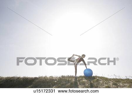A young woman rests her hand on the ball and holds her leg while exercising View Large Photo Image Stock Image - A young woman rests her hand on the ball and holds her leg while exercising. Fotosearch