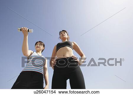 Picture - Low angle view of a young woman holding dumbbell as her mate looks on. Fotosearch