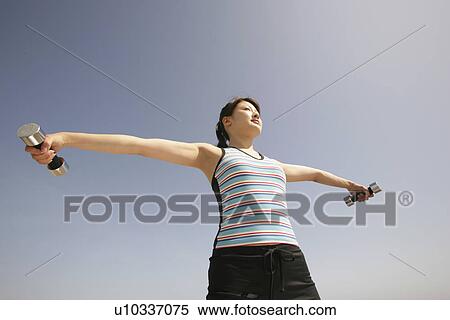 Low angle view of a young woman holding two dumbbells as she stretches her arms View Large Photo Image Stock Photography - Low angle view of a young woman holding two dumbbells as she stretches her arms. Fotosearch