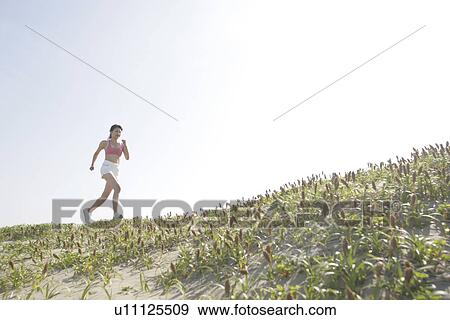 Stock Photo - Side view of a woman jogging during bright sunlight. Fotosearch