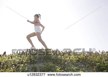 Stock Photo - Side view of a woman jogging during bright sunlight. Fotosearch