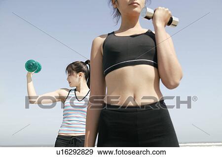 Stock Photo - Two women hold dumbbells under the sky. Fotosearch