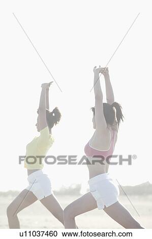 Stock Image - Two young women stretch their arms and legs as they exercise together. Fotosearch