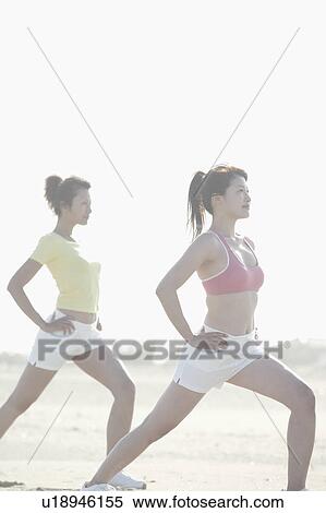 Stock Photography - Two young women stretch their legs as they exercise together. Fotosearch