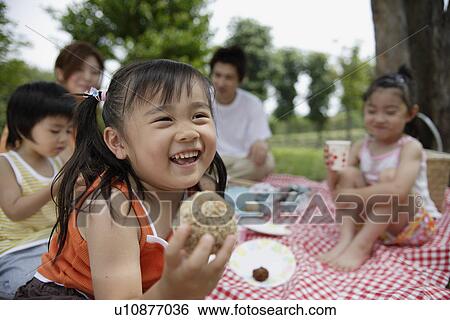 Stock Photograph - A girl having lunch by the trees with her family. Fotosearch