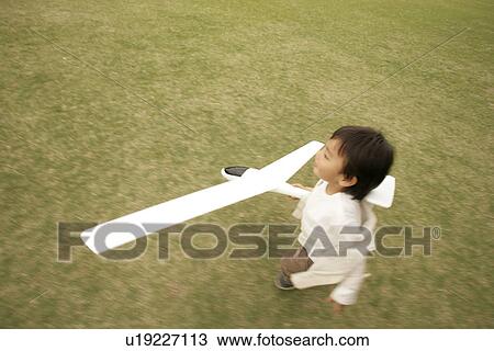 Stock Image - A small boy running on the ground as he holds an aeroplane in his hand. Fotosearch