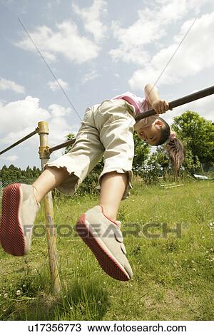 Stock Image - A young girl balancing herself on the rod. Fotosearch