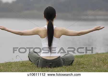 Stock Image - Rear view of a young woman in lotus position. Fotosearch