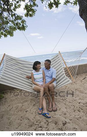 Picture - A couple sitting on hammock. Fotosearch