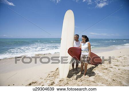 Stock Photo - A couple standing with surfboards at beach. Fotosearch